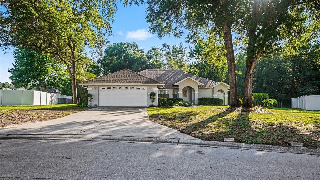 A single-story house with a two-car garage and a concrete driveway sits among mature trees — 6607 SE 11TH LOOP, OCALA, FL