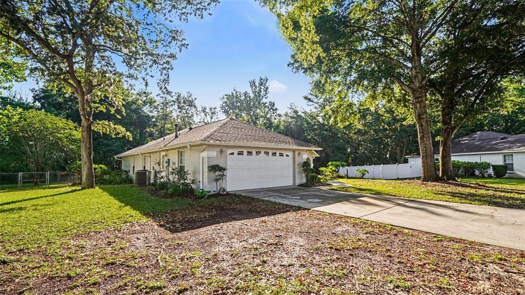 A single-story house with a white garage and driveway sits among large, mature trees — 6607 SE 11TH LOOP, OCALA, FL