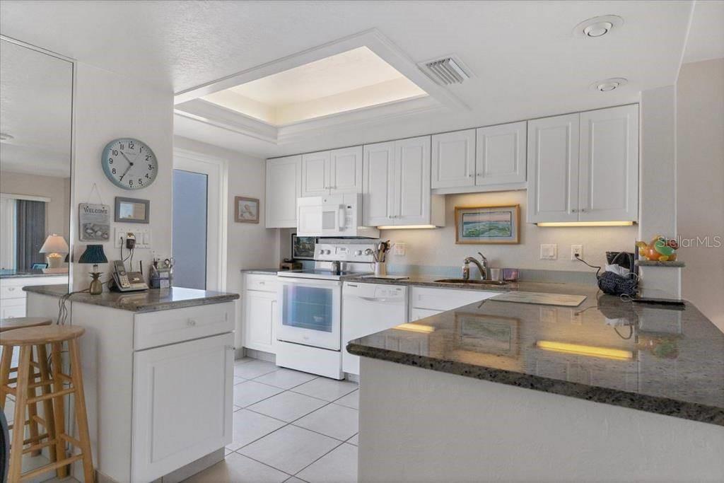A kitchen features white cabinetry, granite countertops, a tiled floor, and a recessed ceiling light — 6154 MIDNIGHT PASS ROAD UNIT 305, SARASOTA, FL