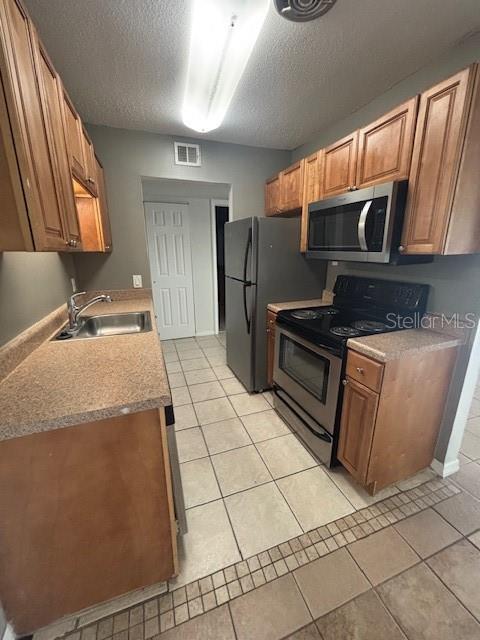 A galley-style kitchen features wood cabinets, stainless steel appliances, and beige tile flooring — 1695 LEE ROAD UNIT B108, WINTER PARK, FL