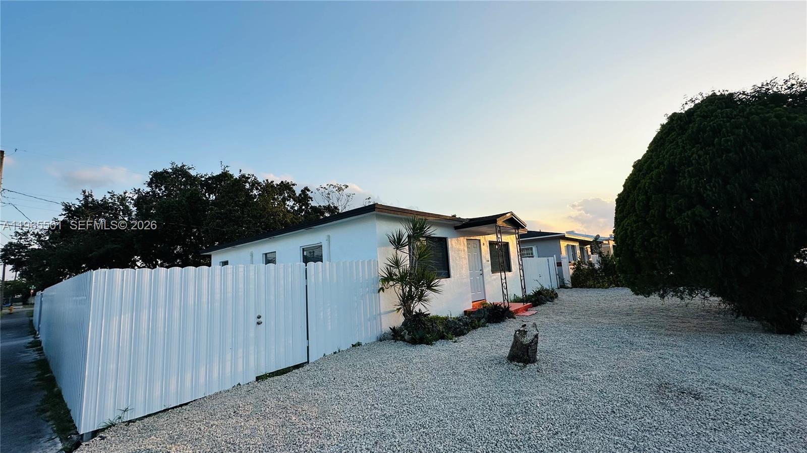 A white single-story house with a gravel yard and a white metal privacy fence — 1100 NW 75th St, Miami FL 33150, MIAMI, FL