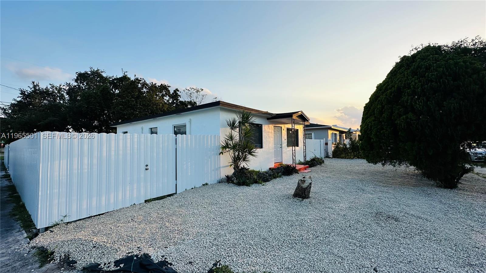 A white single-story house features a gravel yard and a white vinyl privacy fence — 1100 NW 75th St, Miami FL 33150, MIAMI, FL