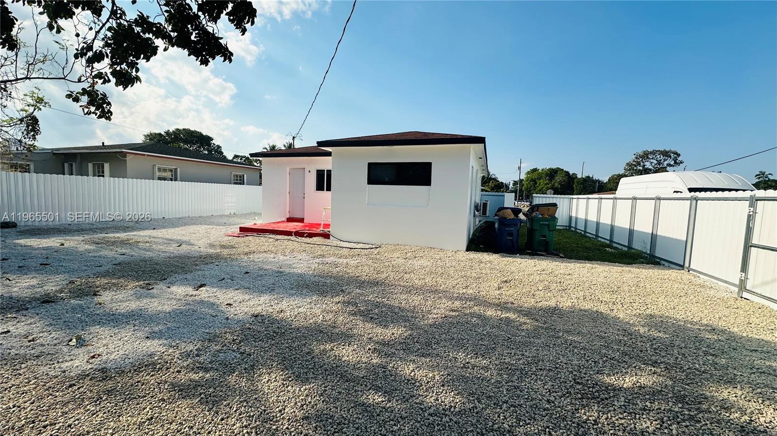 A white house with a red porch sits on a gravel lot enclosed by fencing — 1100 NW 75th St, Miami FL 33150, MIAMI, FL