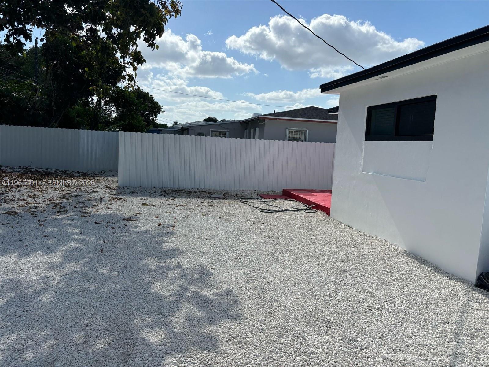A white building stands next to a gravel yard enclosed by a white vinyl fence — 1100 NW 75th St, Miami FL 33150, MIAMI, FL