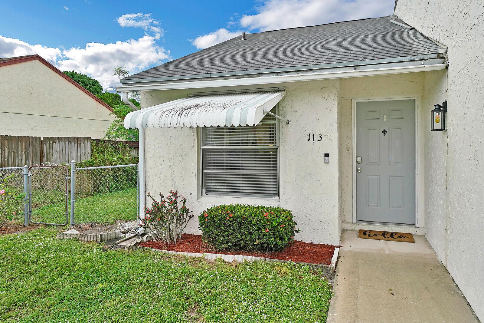 A single-story house exterior features a light-colored stucco facade, a gray door, and an awning — 113 Pinewood Court, Jupiter FL 33458, JUPITER, FL