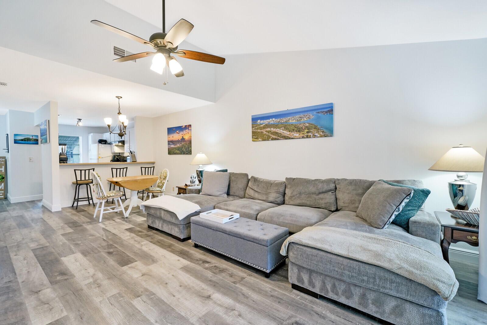A living room with a gray sectional sofa, wood-look flooring, and an open kitchen area — 113 Pinewood Court, Jupiter FL 33458, JUPITER, FL