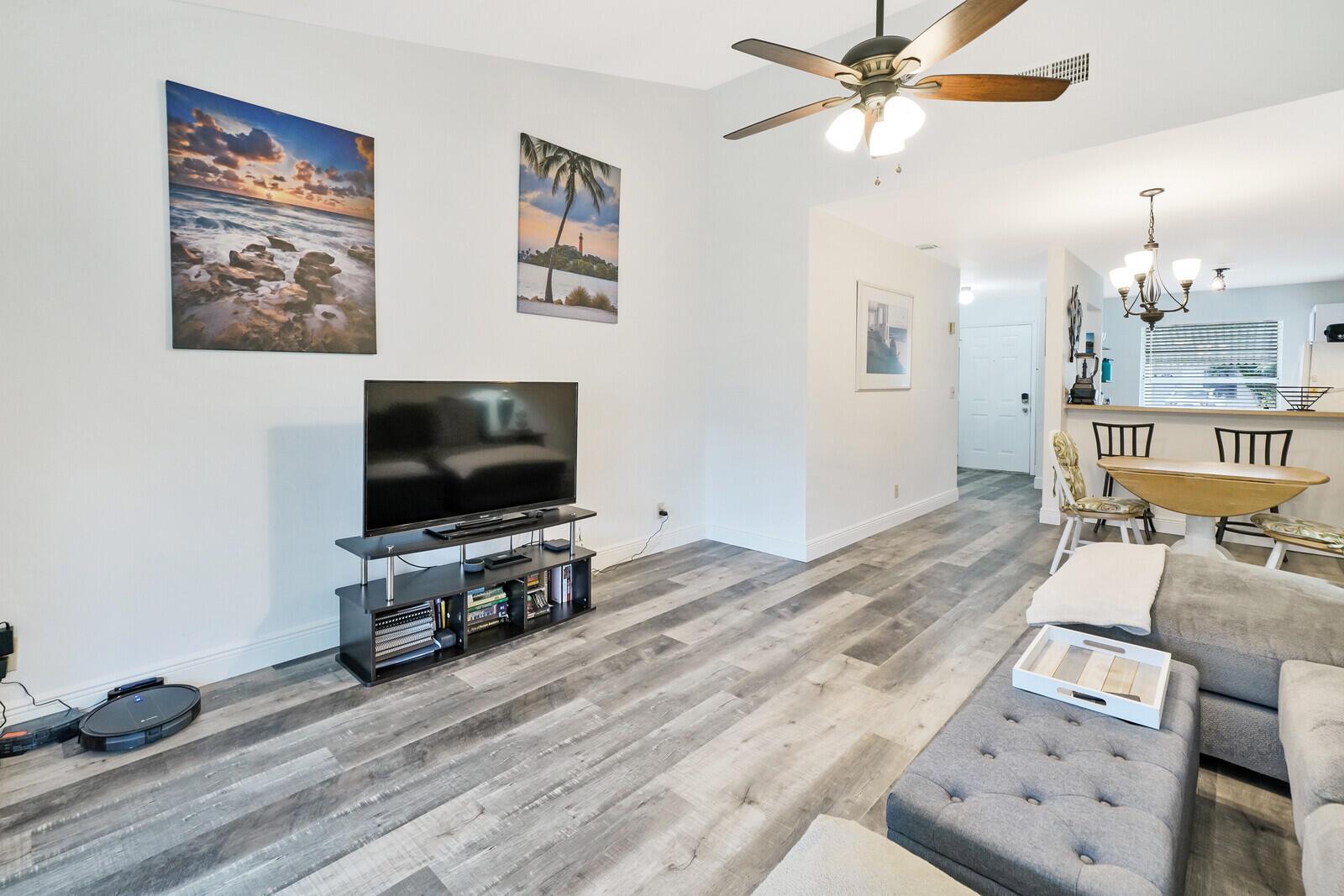 A living room features wood-look flooring, a television on a stand, and a ceiling fan — 113 Pinewood Court, Jupiter FL 33458, JUPITER, FL