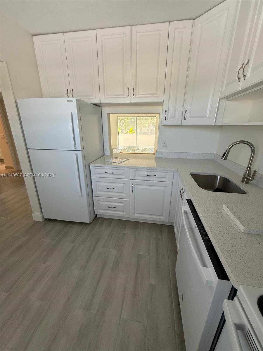 A kitchen features white cabinets, light-colored countertops, a stainless steel sink, and light wood flooring — 7200 NW 4th Pl # 201, Margate FL 33063, MARGATE, FL