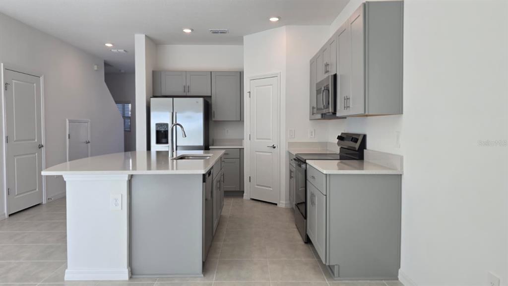 A modern kitchen features gray cabinets, white countertops, a central island, and stainless steel appliances — 2220 PORTRAIT STREET, POINCIANA, FL