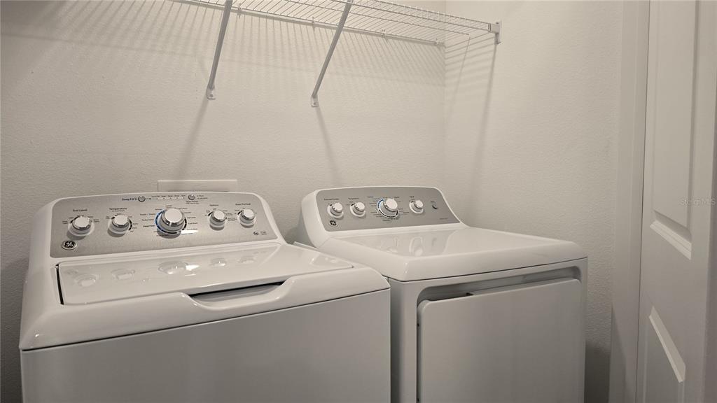 A laundry room features a white top-load washing machine and dryer beneath a wire shelf — 2220 PORTRAIT STREET, POINCIANA, FL