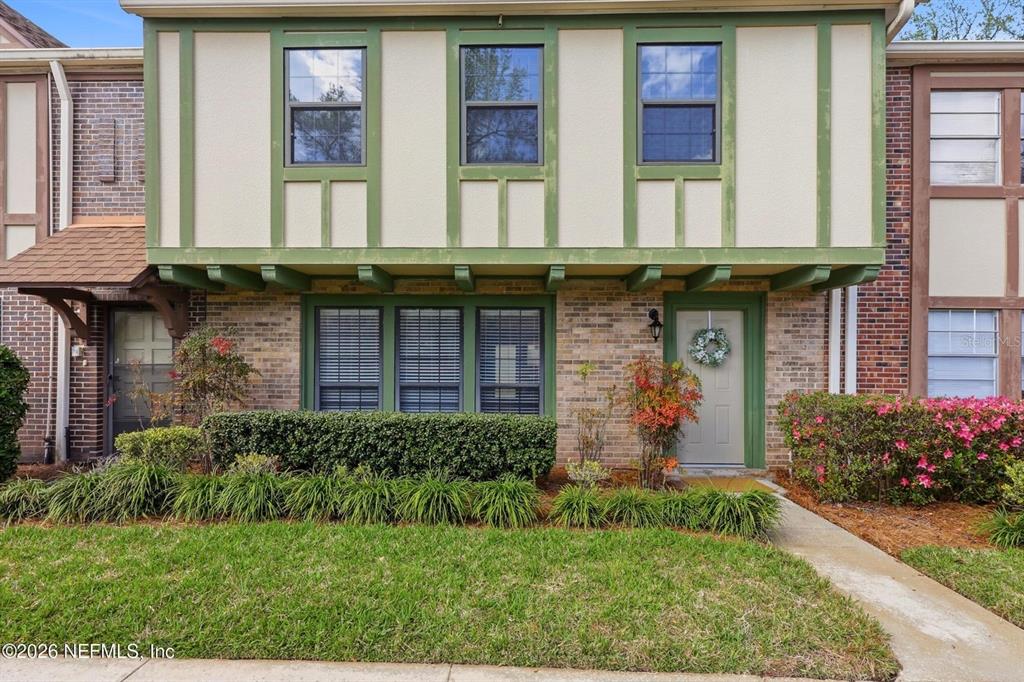 A two-story townhouse with brick and stucco siding, green trim, and a small front garden — 8153 SUTTON PLACE N, JACKSONVILLE, FL