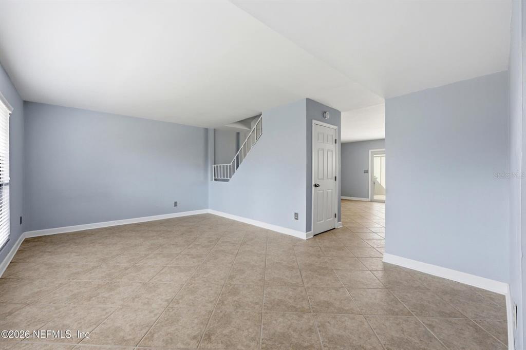 An empty room features light blue walls, beige tile flooring, and a white staircase — 8153 SUTTON PLACE N, JACKSONVILLE, FL