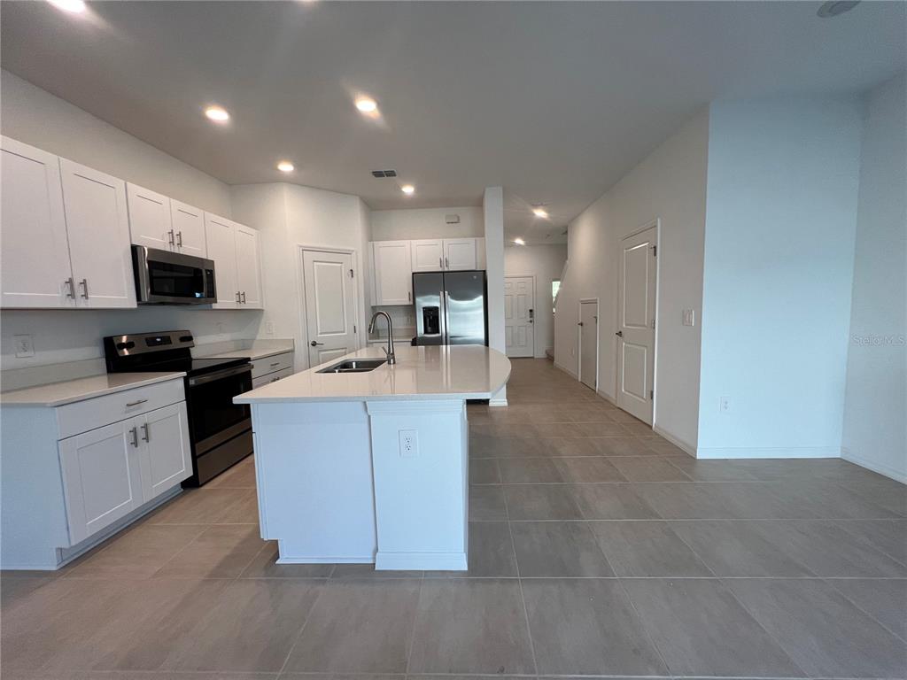 A modern kitchen features white cabinets, stainless steel appliances, a center island, and tile flooring — 2211 PORTRAIT STREET, KISSIMMEE, FL