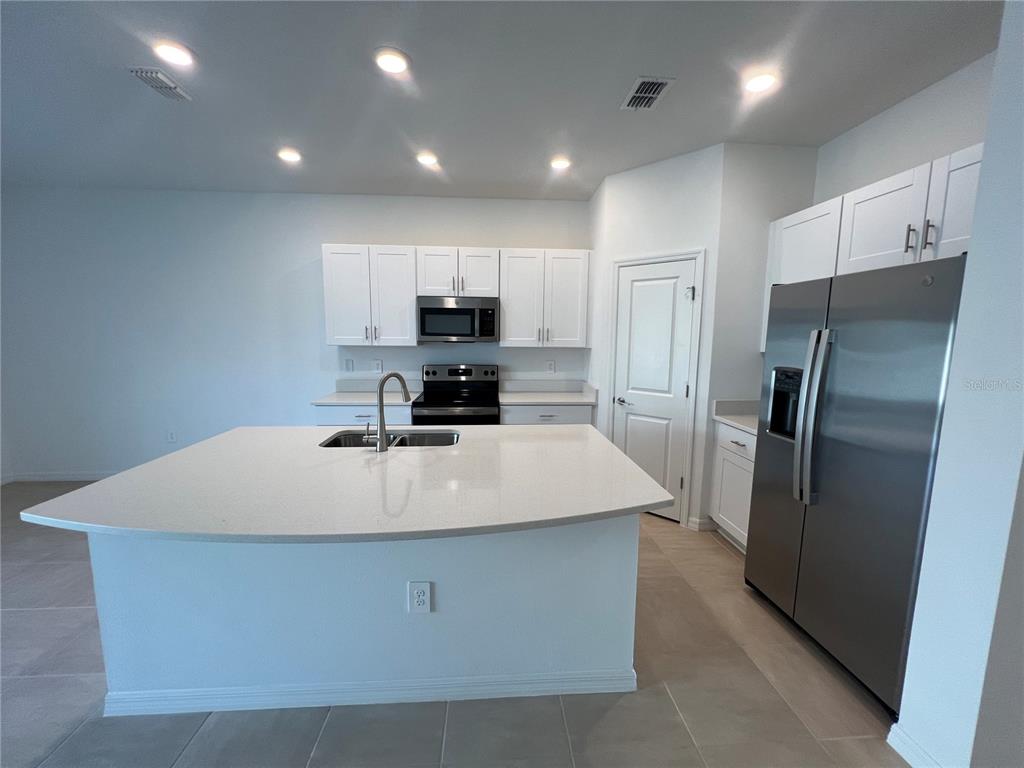 A modern kitchen features white cabinets, stainless steel appliances, and a large quartz-topped island — 2211 PORTRAIT STREET, KISSIMMEE, FL