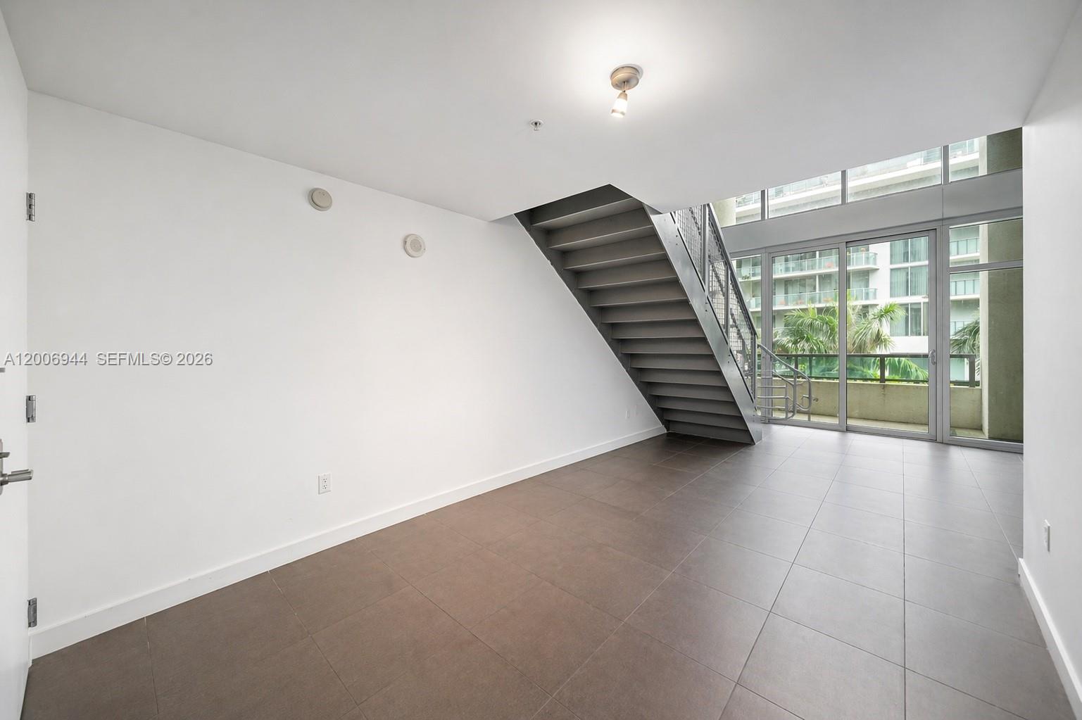 An empty room features large floor tiles, a metal staircase, and floor-to-ceiling glass doors — 3301 NE 1st Ave # M0308, Miami FL 33137, MIAMI, FL