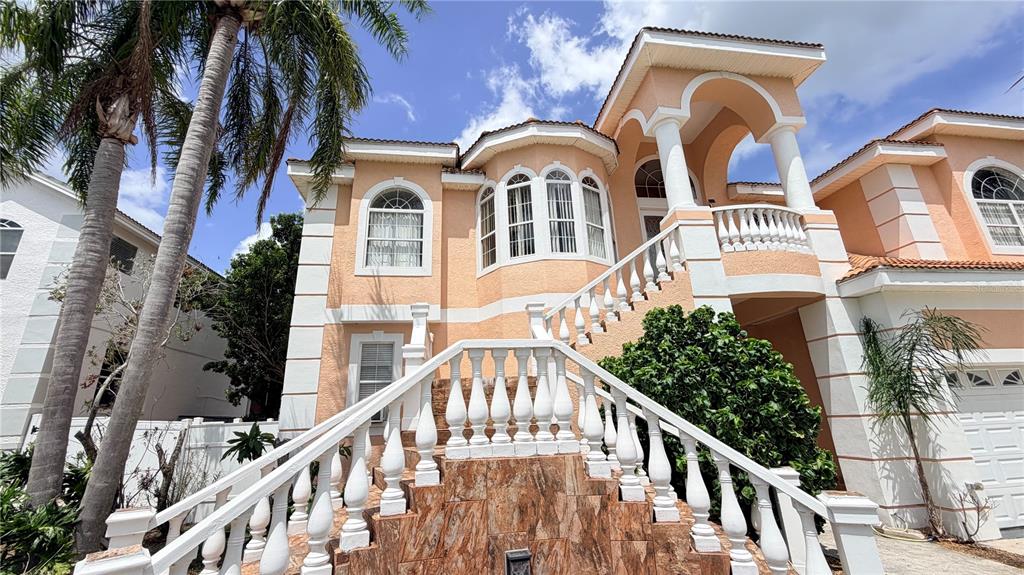A peach-colored two-story house features a prominent stone-tiled staircase with white balustrades — 3187 SHORELINE DRIVE, CLEARWATER, FL