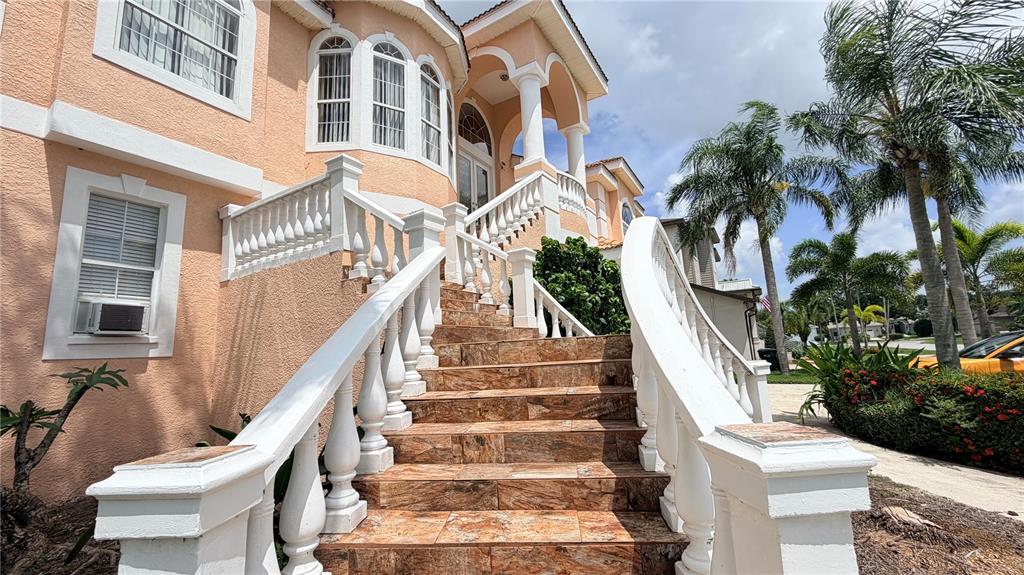 An exterior view of a peach-colored house with a tiled staircase and white balustrades — 3187 SHORELINE DRIVE, CLEARWATER, FL