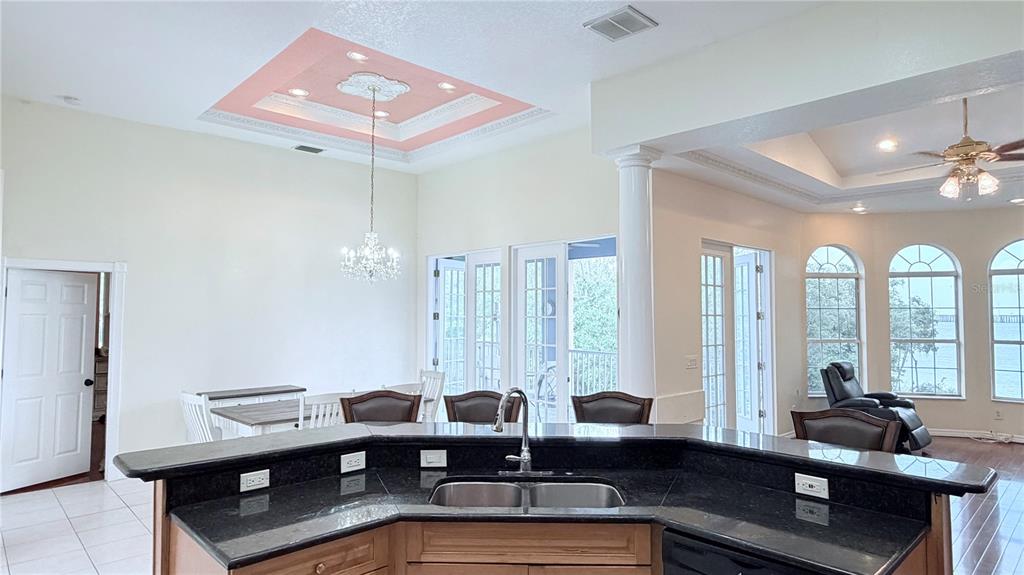 A kitchen island with a black countertop overlooks a dining area with a pink tray ceiling — 3187 SHORELINE DRIVE, CLEARWATER, FL