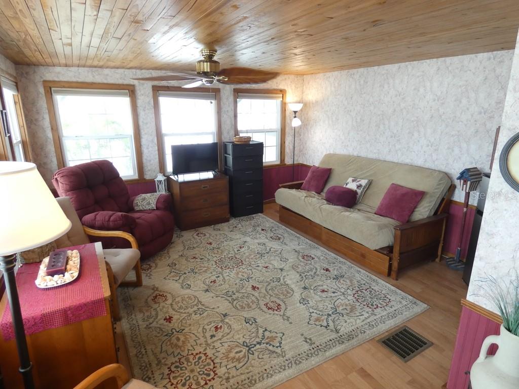 A living room features a wood-paneled ceiling, floral wallpaper, a futon, and a patterned rug — 12674 SEMINOLE BOULEVARD UNIT S8, LARGO, FL