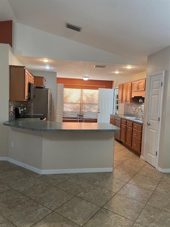 A kitchen features wood cabinets, a breakfast bar, tile flooring, and a vaulted ceiling — 4258 ORCHID BOULEVARD, LAKE WALES, FL