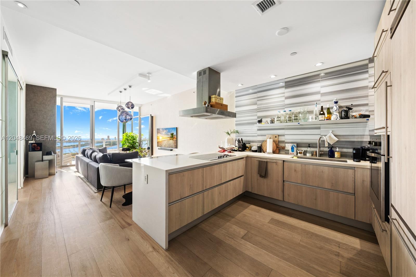 A modern kitchen with light wood cabinets and a white island overlooks a living area — 1100 Biscayne Blvd # 5004, Miami FL 33132, MIAMI, FL