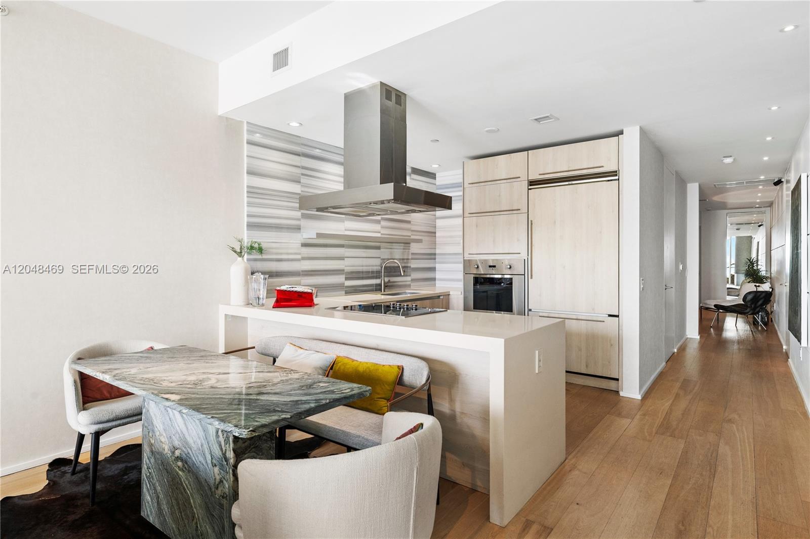 A modern kitchen features light wood cabinetry, a stone island, and a marble dining table — 1100 Biscayne Blvd # 5004, Miami FL 33132, MIAMI, FL