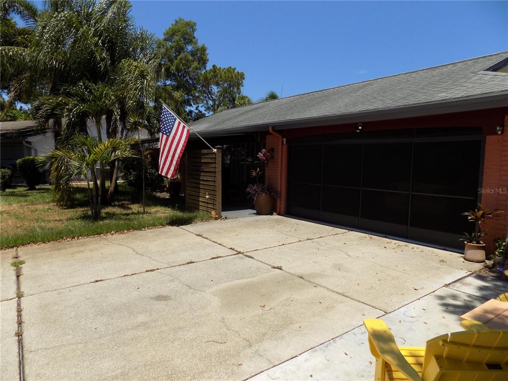 A concrete driveway leads to a house with a screened-in garage and an American flag — 3849 EDGEMONT DRIVE, NEW PORT RICHEY, FL