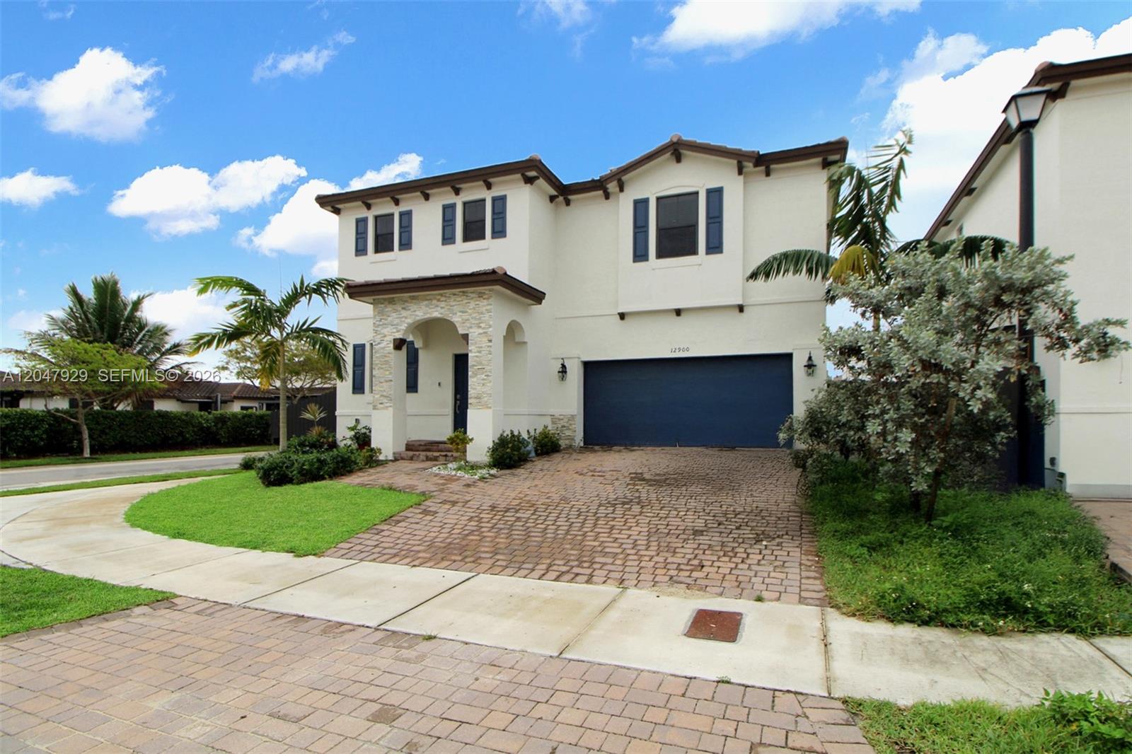 A two-story house with a stone-accented entryway, blue garage door, and paver driveway — 12900 SW 229th St, Miami FL 33170, MIAMI, FL