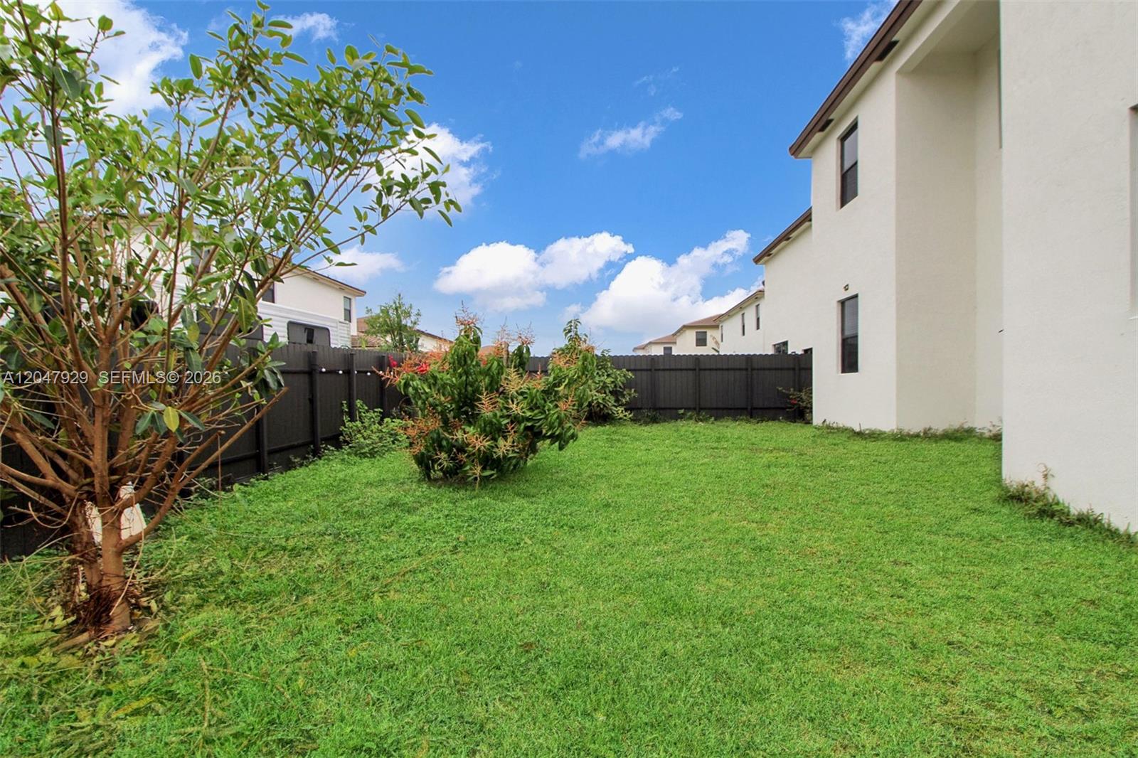 A grassy backyard features a small tree, a central shrub, and a dark wooden fence — 12900 SW 229th St, Miami FL 33170, MIAMI, FL