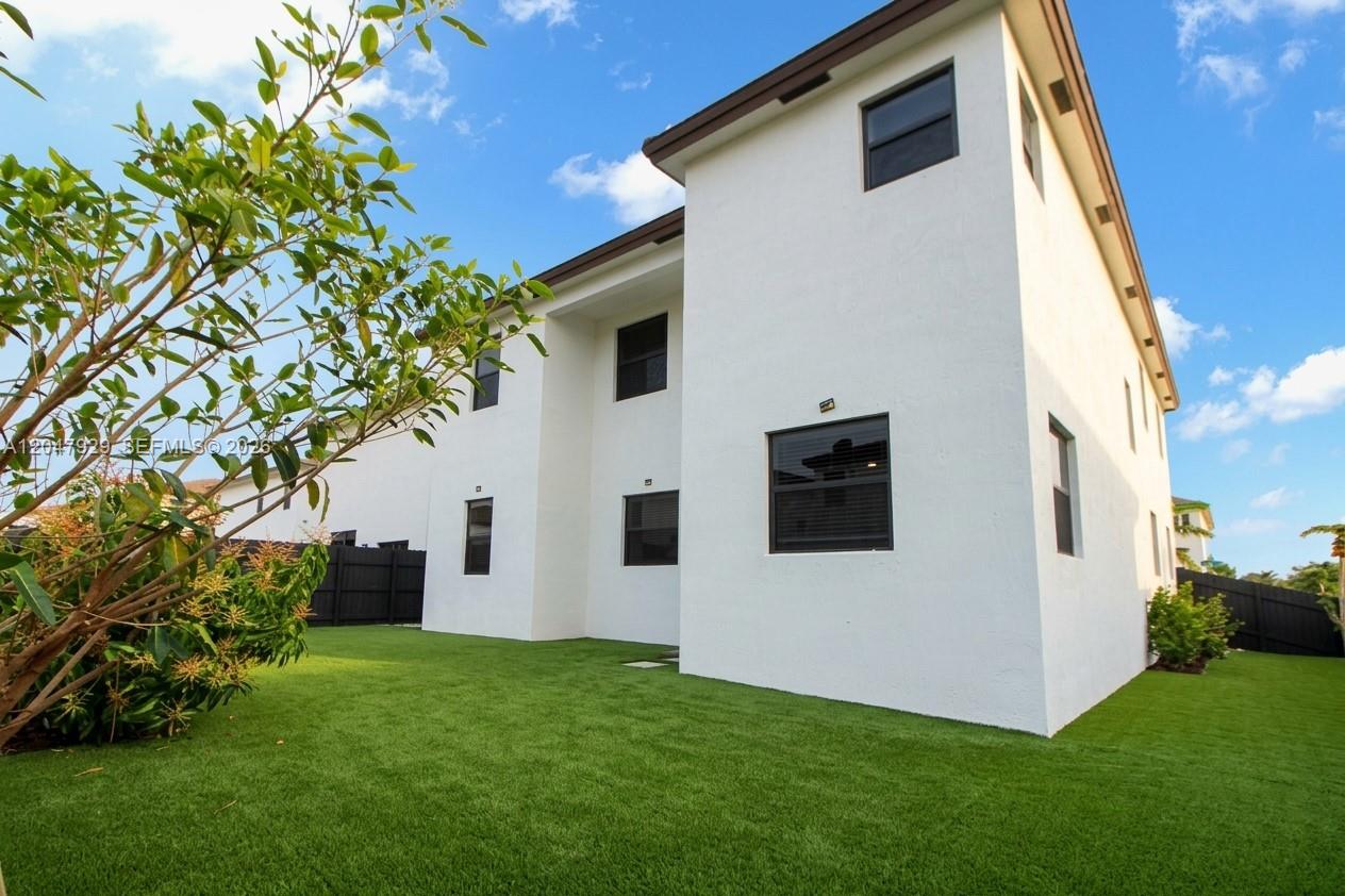 The exterior of a two-story white house features a green artificial turf backyard — 12900 SW 229th St, Miami FL 33170, MIAMI, FL
