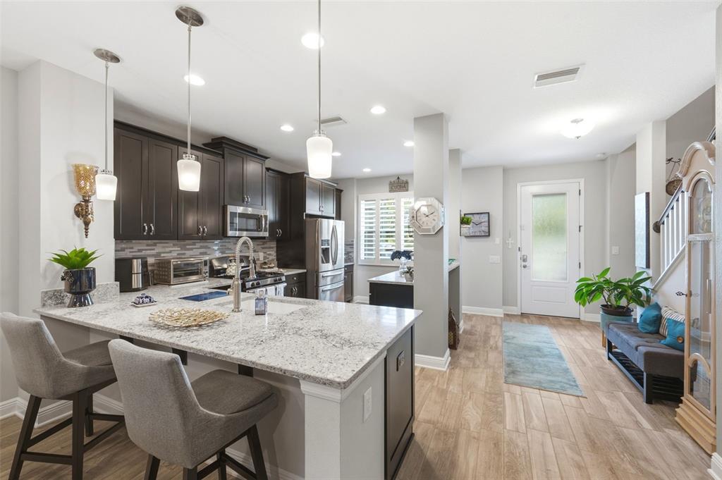 A kitchen features dark cabinetry, granite countertops, a breakfast bar, and an adjacent entryway area — 13011 BATTEN LANE, ODESSA, FL