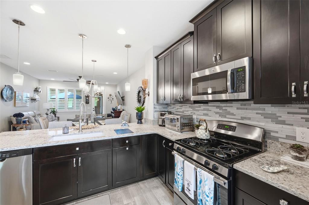 A kitchen with dark wood cabinets, granite countertops, and stainless steel appliances overlooks a living area — 13011 BATTEN LANE, ODESSA, FL