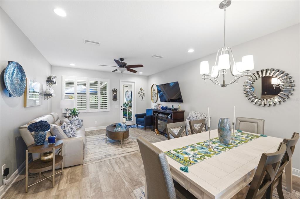 An open-concept living and dining room with light wood-look flooring and a modern chandelier — 13011 BATTEN LANE, ODESSA, FL
