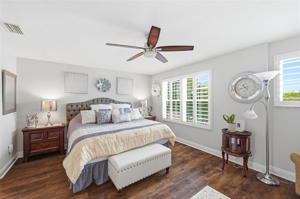 A bedroom features a tufted headboard, wood flooring, a ceiling fan, and plantation shutters — 13011 BATTEN LANE, ODESSA, FL