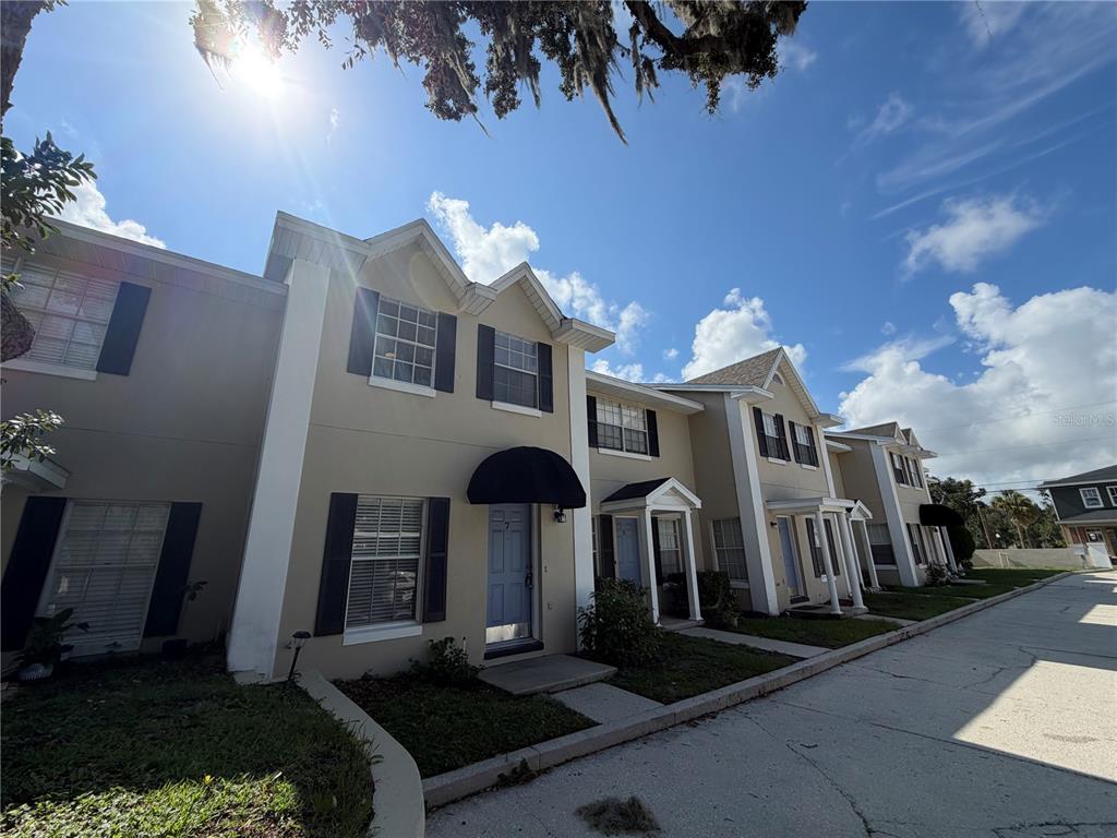 A row of two-story townhomes with beige stucco siding and dark shutters under a sunny sky — 850 E LIME STREET UNIT 7, LAKELAND, FL