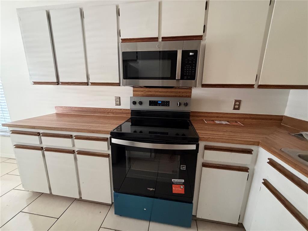 A kitchen features white cabinets, wood-look laminate countertops, and a stainless steel stove and microwave — 850 E LIME STREET UNIT 7, LAKELAND, FL