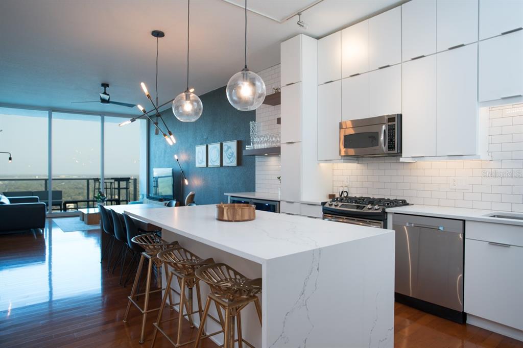 A modern kitchen with white cabinets, a quartz island, and gold bar stools overlooks a balcony — 150 E ROBINSON STREET UNIT 2209, ORLANDO, FL