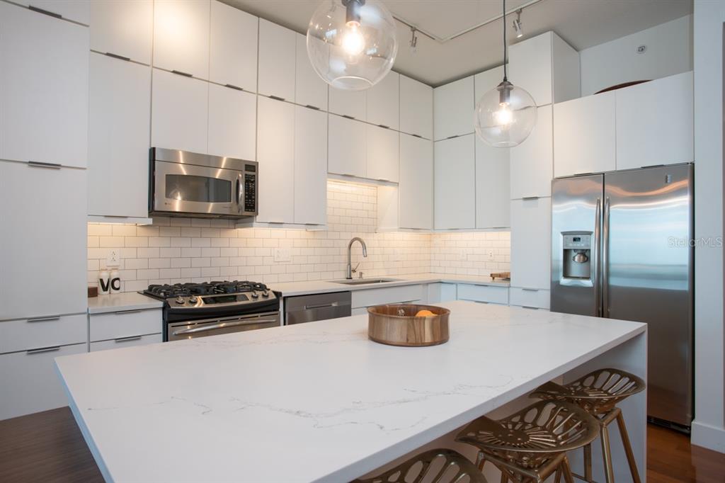 A modern kitchen features white flat-panel cabinets, stainless steel appliances, and a large marble island — 150 E ROBINSON STREET UNIT 2209, ORLANDO, FL