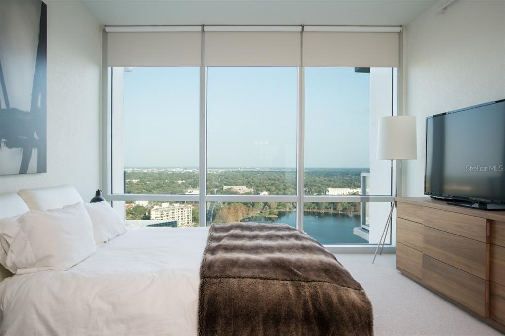 A bedroom with a bed, a television on a dresser, and floor-to-ceiling windows overlooking water — 150 E ROBINSON STREET UNIT 2209, ORLANDO, FL