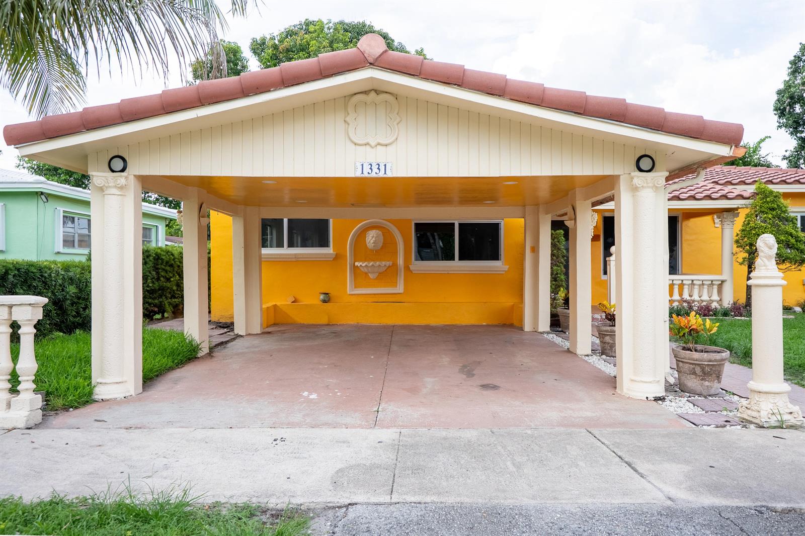 A bright yellow house features a covered carport with decorative columns and a wall fountain — 1331 NW 87th Street, Miami FL 33147, MIAMI, FL