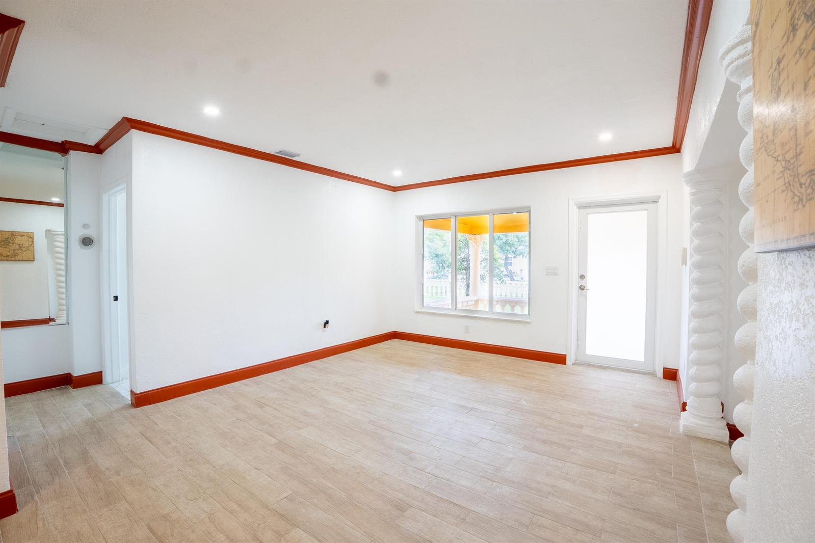 An empty room with white walls, orange crown molding, wood-look tile floors, and decorative columns — 1331 NW 87th Street, Miami FL 33147, MIAMI, FL