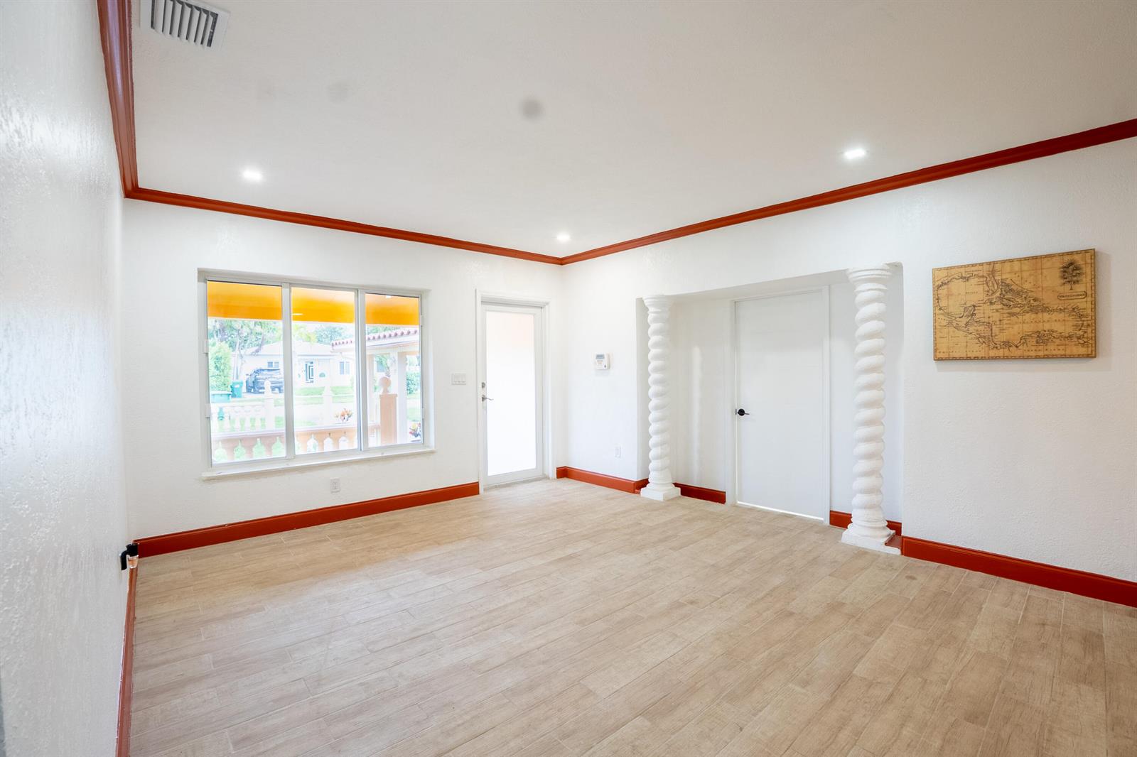 An empty room features white walls, reddish-brown trim, light wood-look tile flooring, and decorative columns — 1331 NW 87th Street, Miami FL 33147, MIAMI, FL