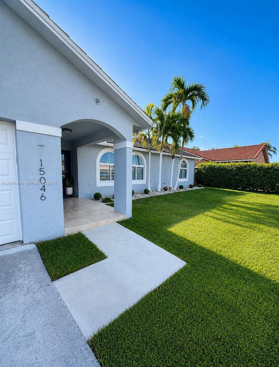 A light blue house exterior features an arched entryway, a concrete walkway, and palm trees — 15046 SW 148th Pl, Miami FL 33196, MIAMI, FL