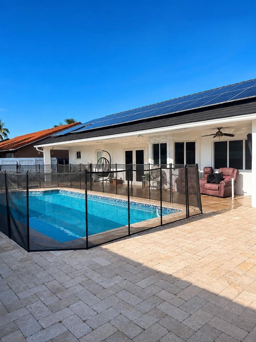 A backyard features a swimming pool with a safety fence and solar panels on the roof — 15046 SW 148th Pl, Miami FL 33196, MIAMI, FL
