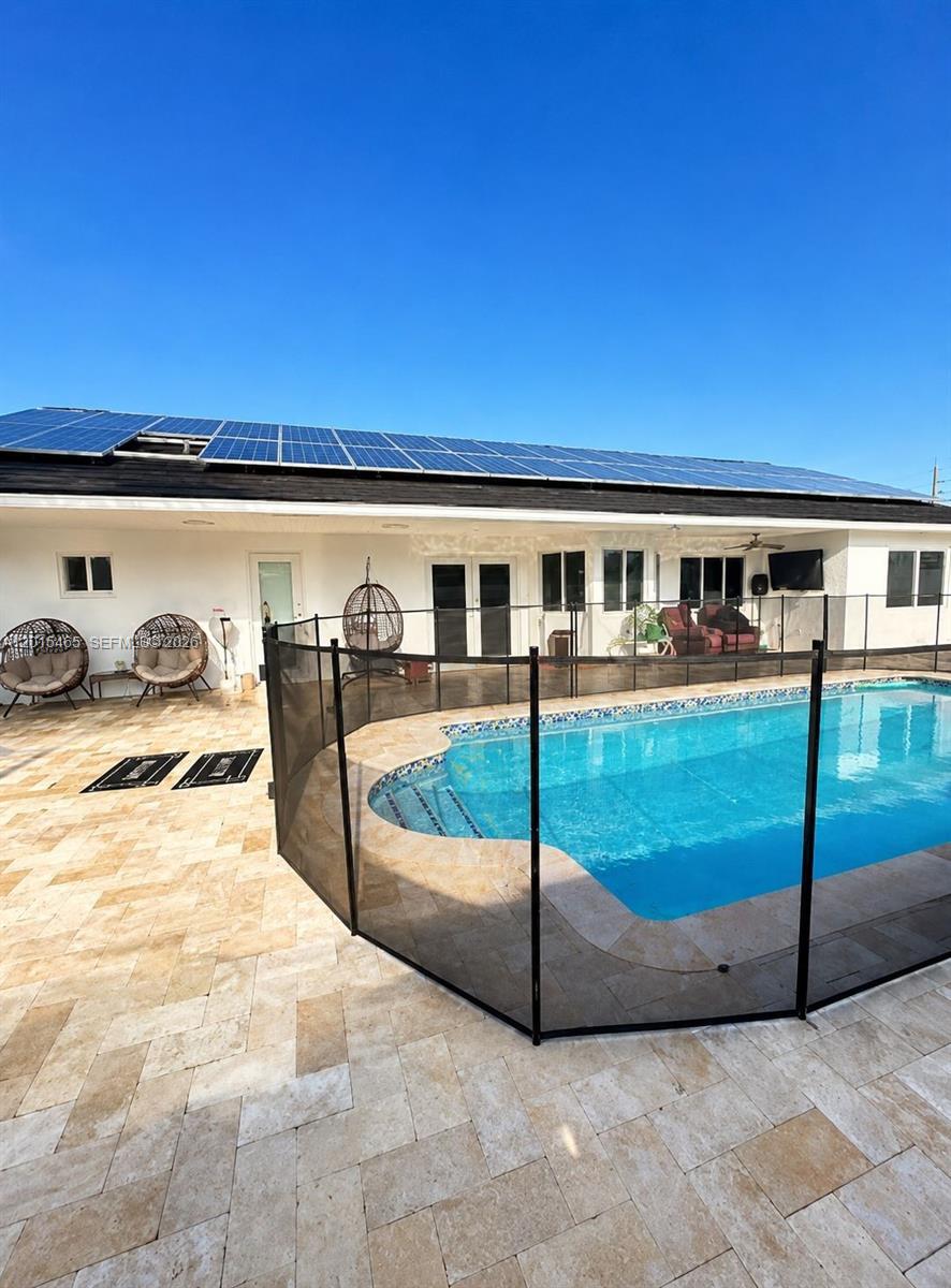 A swimming pool with a black safety fence sits on a stone patio behind a house — 15046 SW 148th Pl, Miami FL 33196, MIAMI, FL