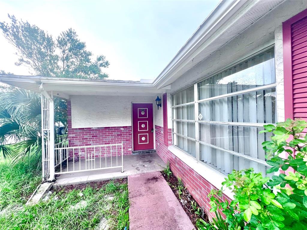 A front exterior view showing a covered porch, a pink door, and brick siding — 7204 ISLE DRIVE, PORT RICHEY, FL