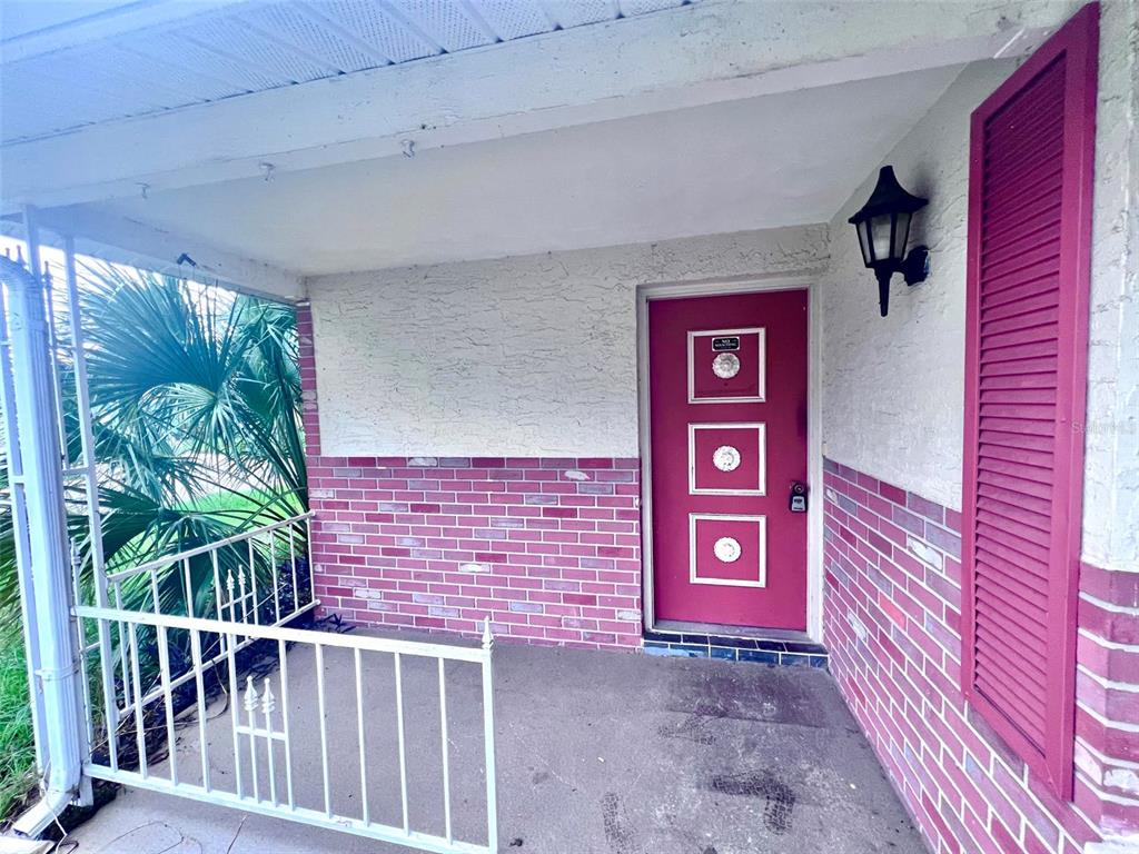 A covered porch features a red front door with three square windows and brick siding — 7204 ISLE DRIVE, PORT RICHEY, FL