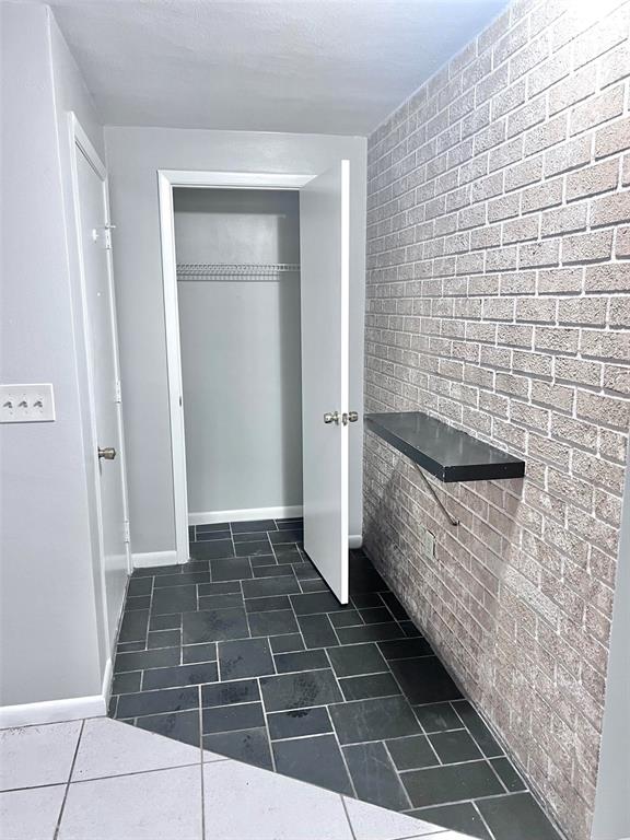 A hallway features dark slate tile flooring, a brick accent wall with a shelf, and closets — 7204 ISLE DRIVE, PORT RICHEY, FL