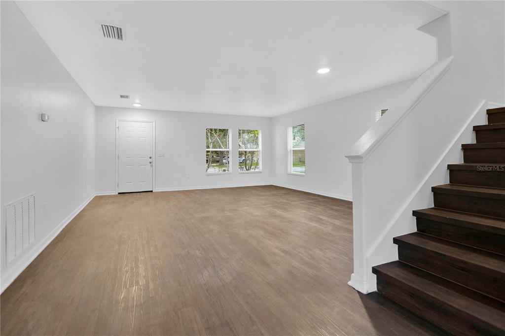 An empty living room features light-colored walls, wood-look flooring, and a dark wood staircase — 10414 BOYETTE CREEK BOULEVARD, RIVERVIEW, FL