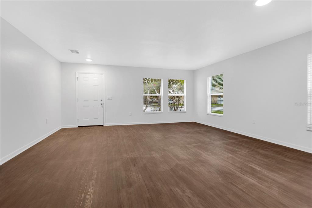 An empty room features light gray walls, wood-look flooring, a white door, and three windows — 10414 BOYETTE CREEK BOULEVARD, RIVERVIEW, FL